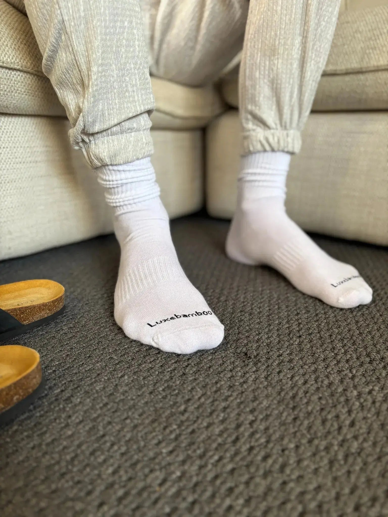 White bamboo socks with a brand logo luxebamboo worn by a person sitting on a couch.